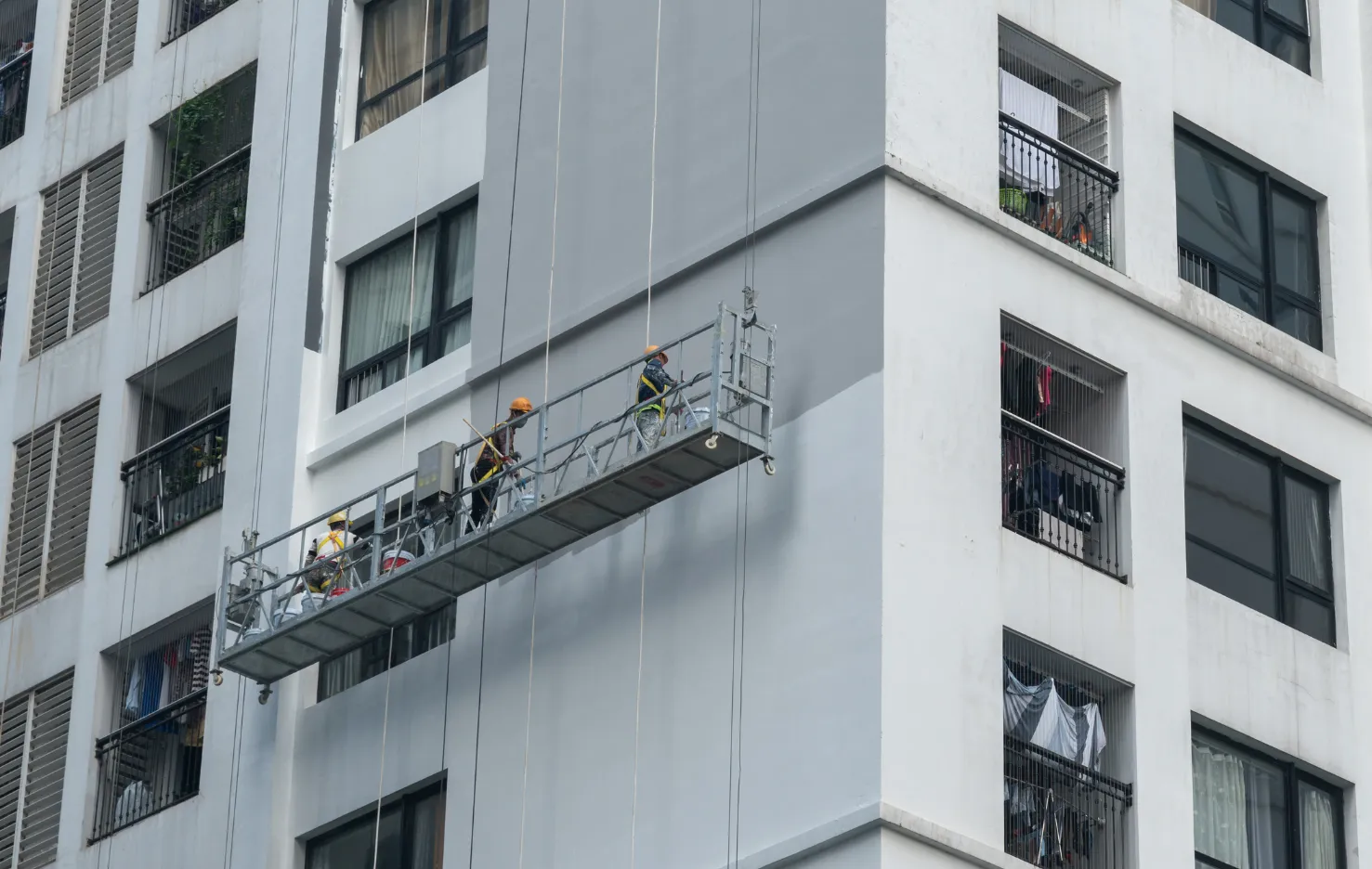 Workers on a suspended platform cleaning tall building windows.