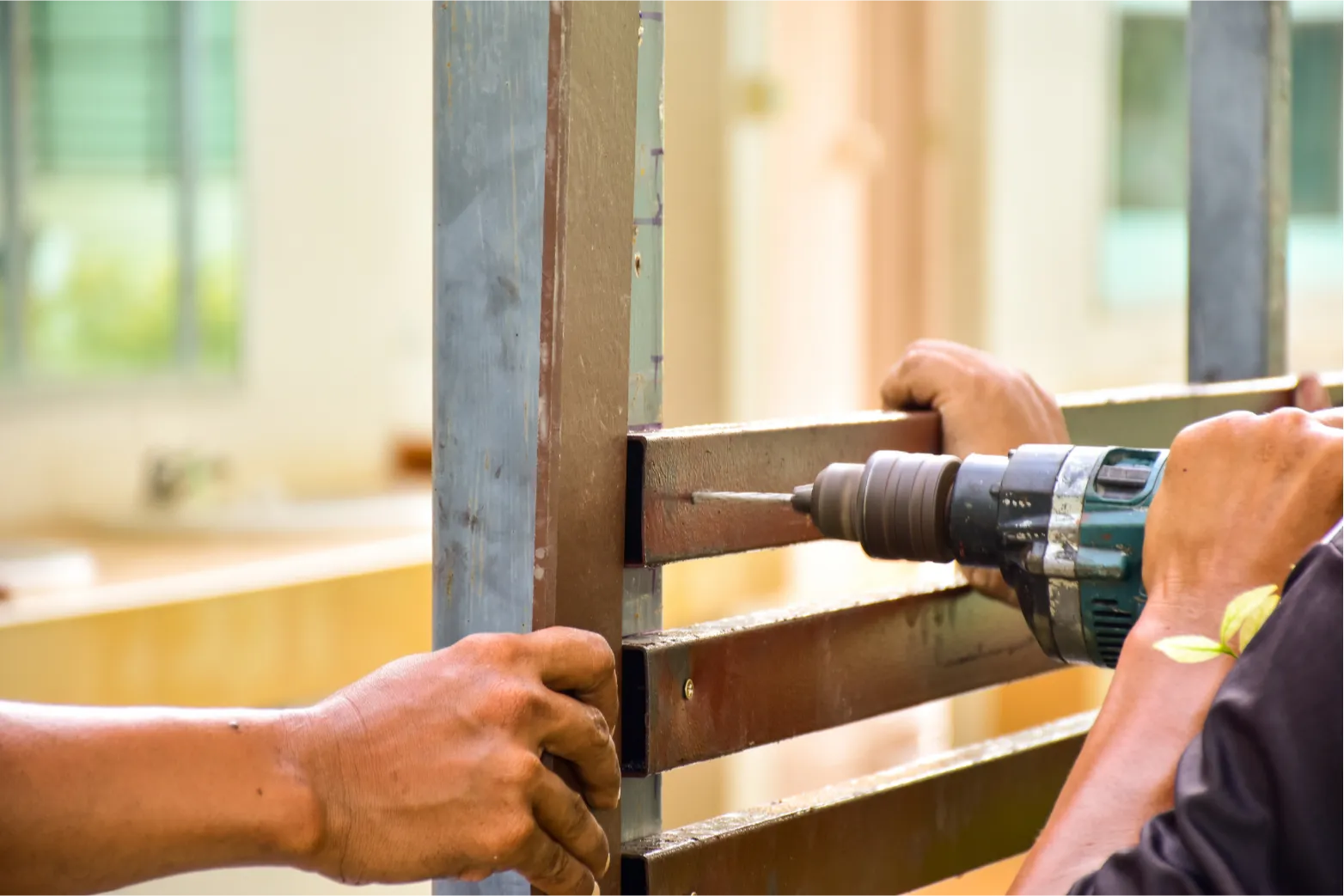 fence-repair-3 Two people working with a power drill on a metal frame indoors.