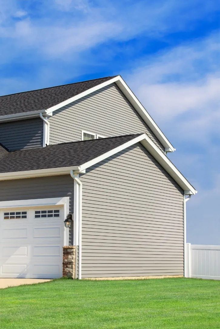 siding-installation-2 Modern two-story house with gray siding, dark roof, and attached white garage. Green lawn and blue sky in the background.