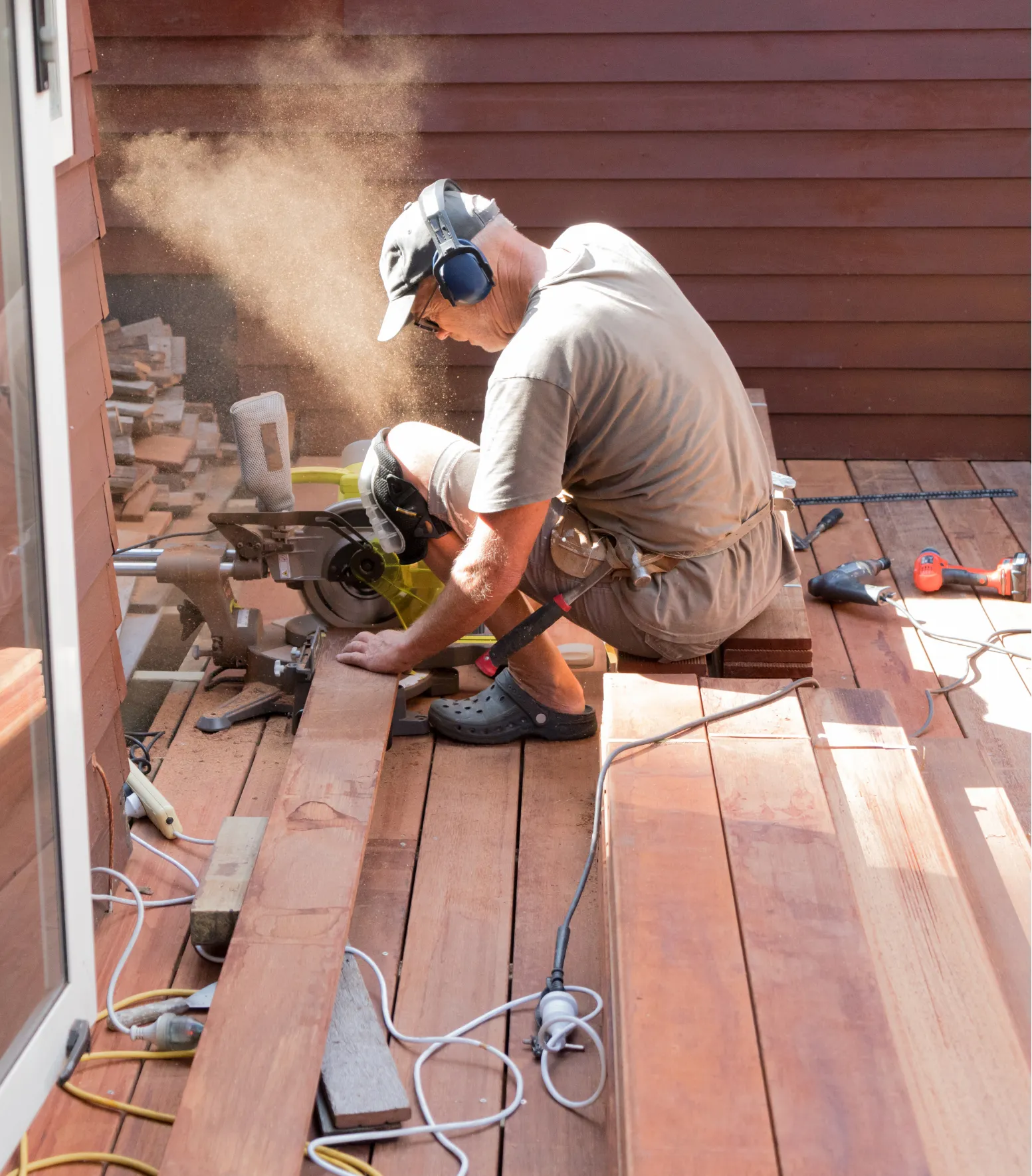 why-hire-a-professional Man in protective gear cuts wood on a deck with a power saw; sawdust fills the air.