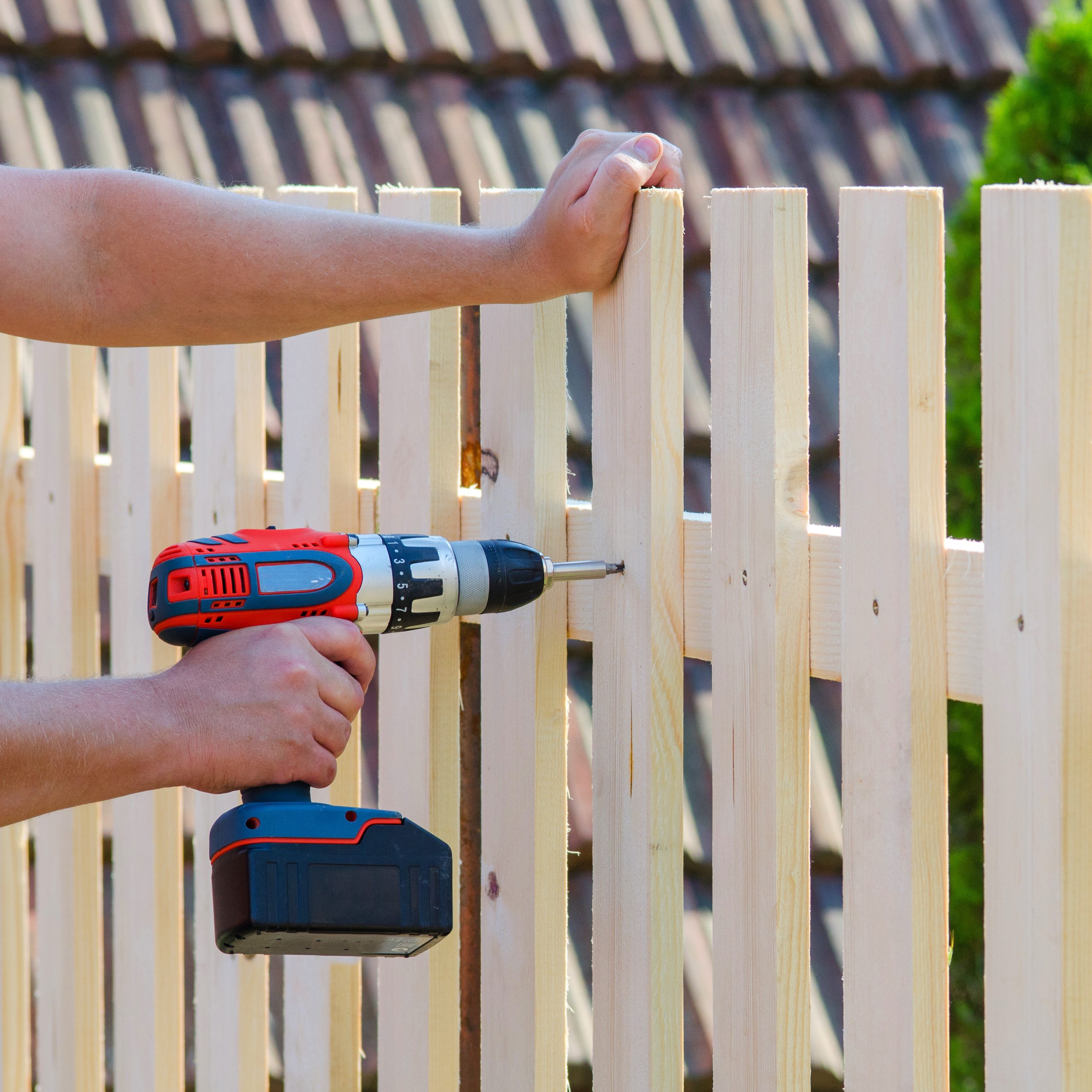Person using a cordless drill to secure planks on a wooden fence.