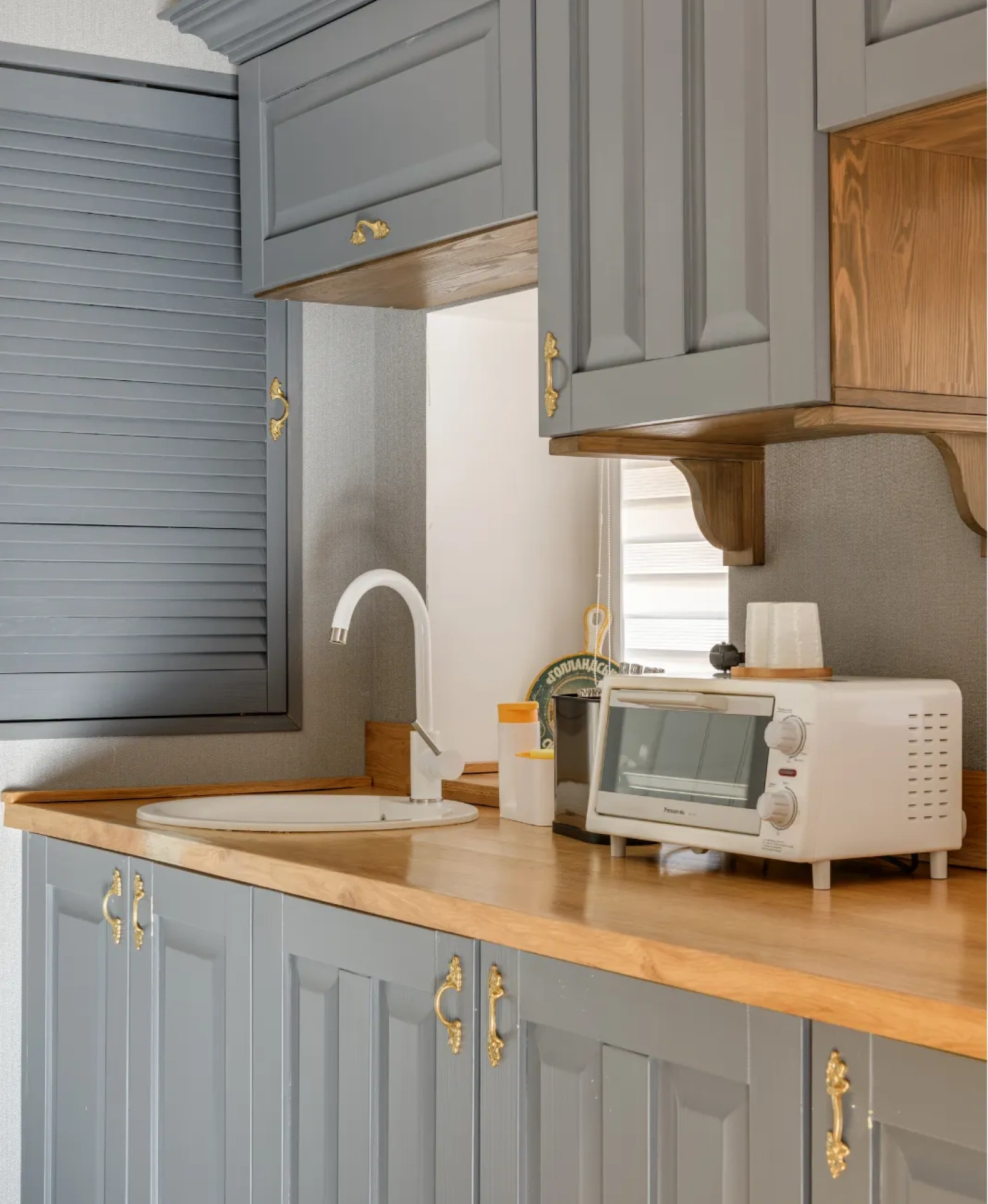 A compact kitchen with gray cabinets, a wooden countertop, a white sink, and a small white toaster oven.