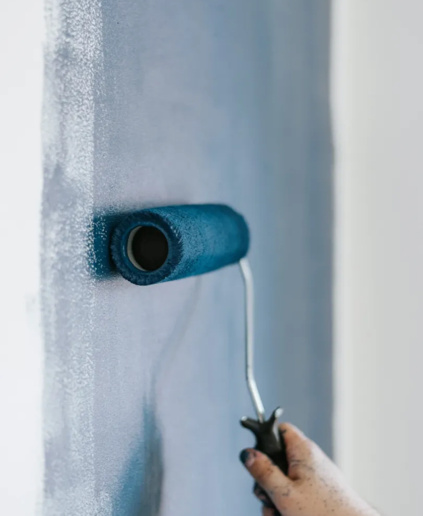 commercial-1 A hand painting a wall with blue paint using a roller brush.