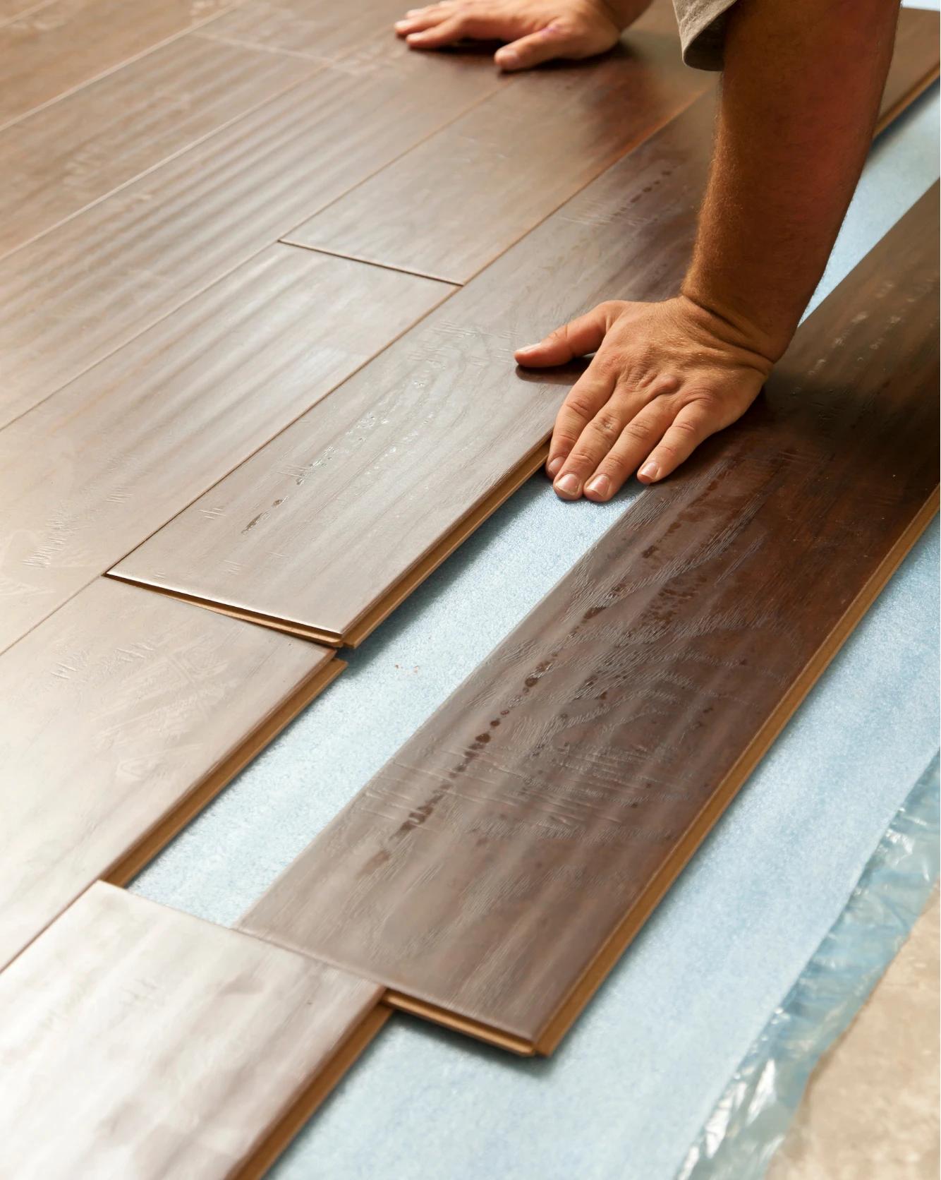 flooring-5 A person installing dark wood laminate flooring, pressing planks together over a foam underlayment.