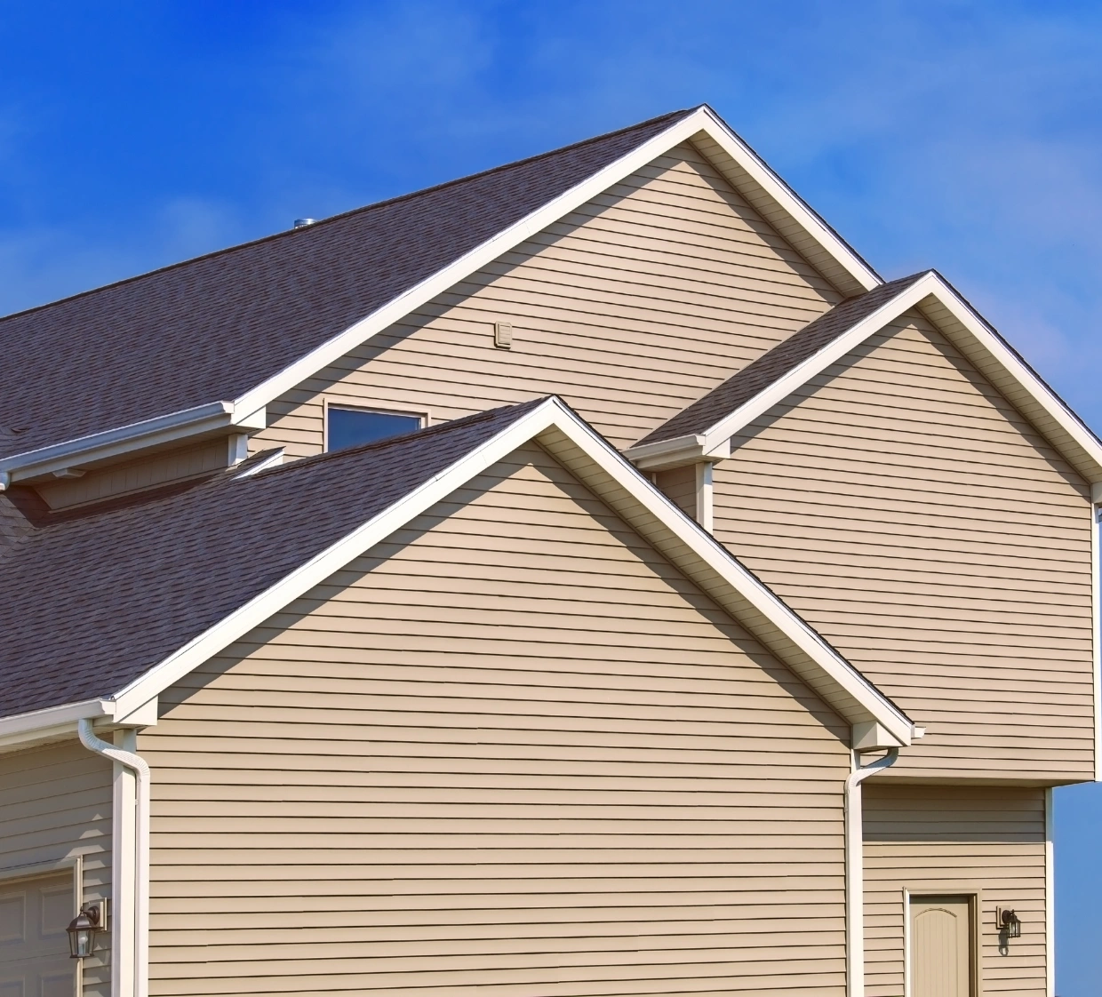siding-2 Beige suburban house with gable roofs and white trim under a clear blue sky.