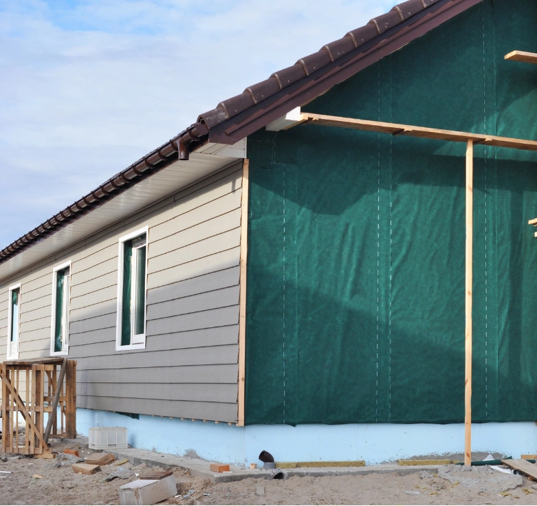 siding-rep-1 Partially completed house with beige siding and a green weatherproof barrier, under construction.
