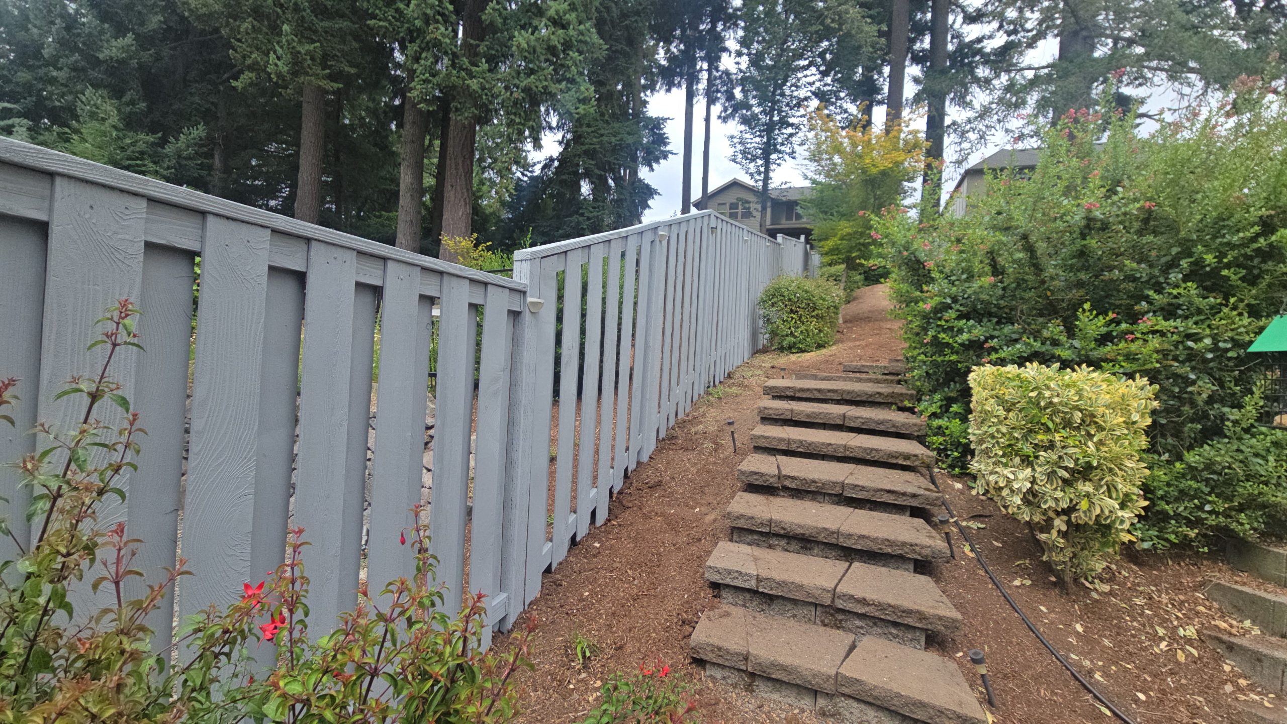 Stone steps leading up a dirt path alongside a grey wooden fence.
