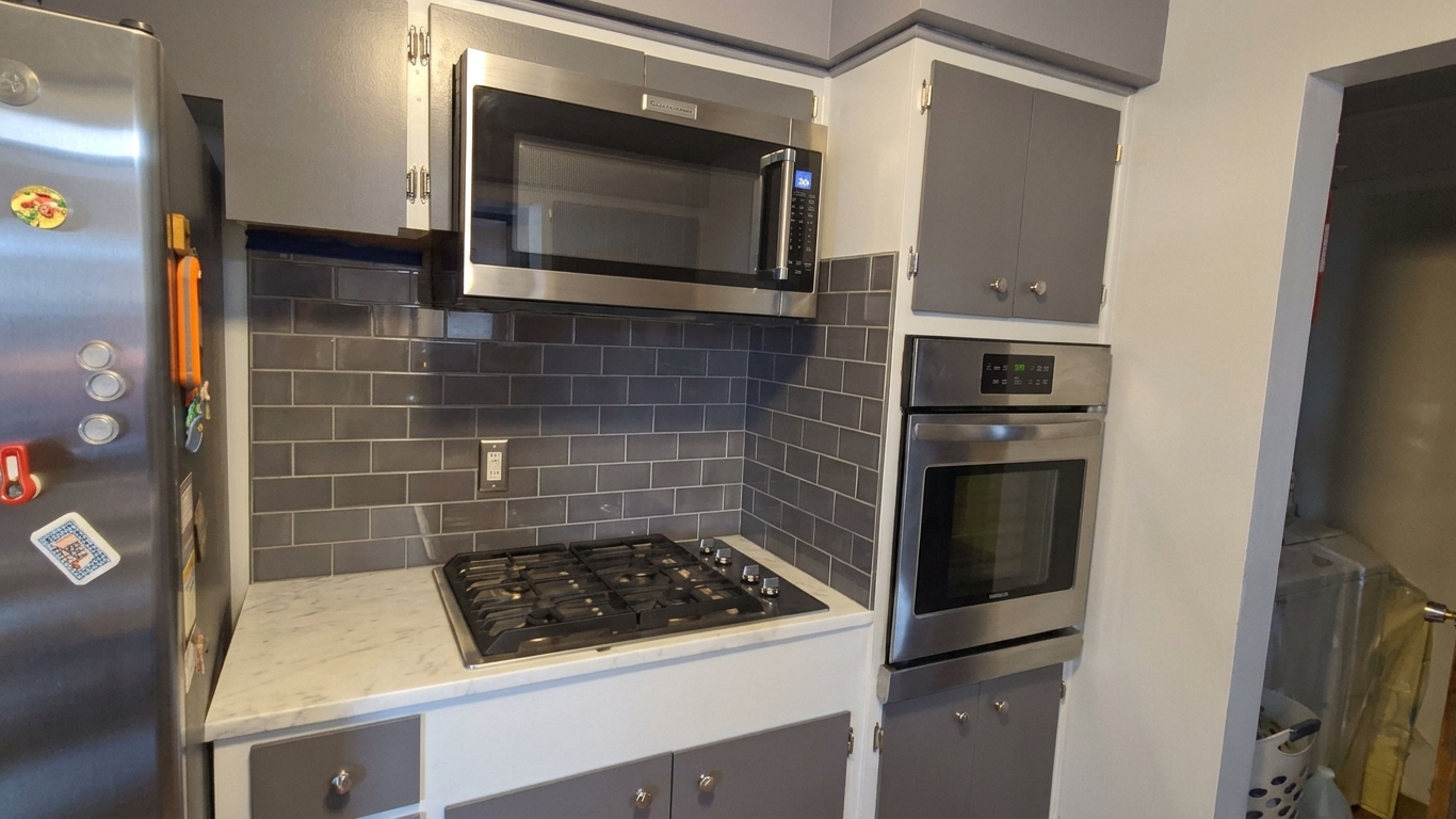 Kitchen area with a gas stovetop, microwave, wall oven, gray cabinets, and a gray tile backsplash.