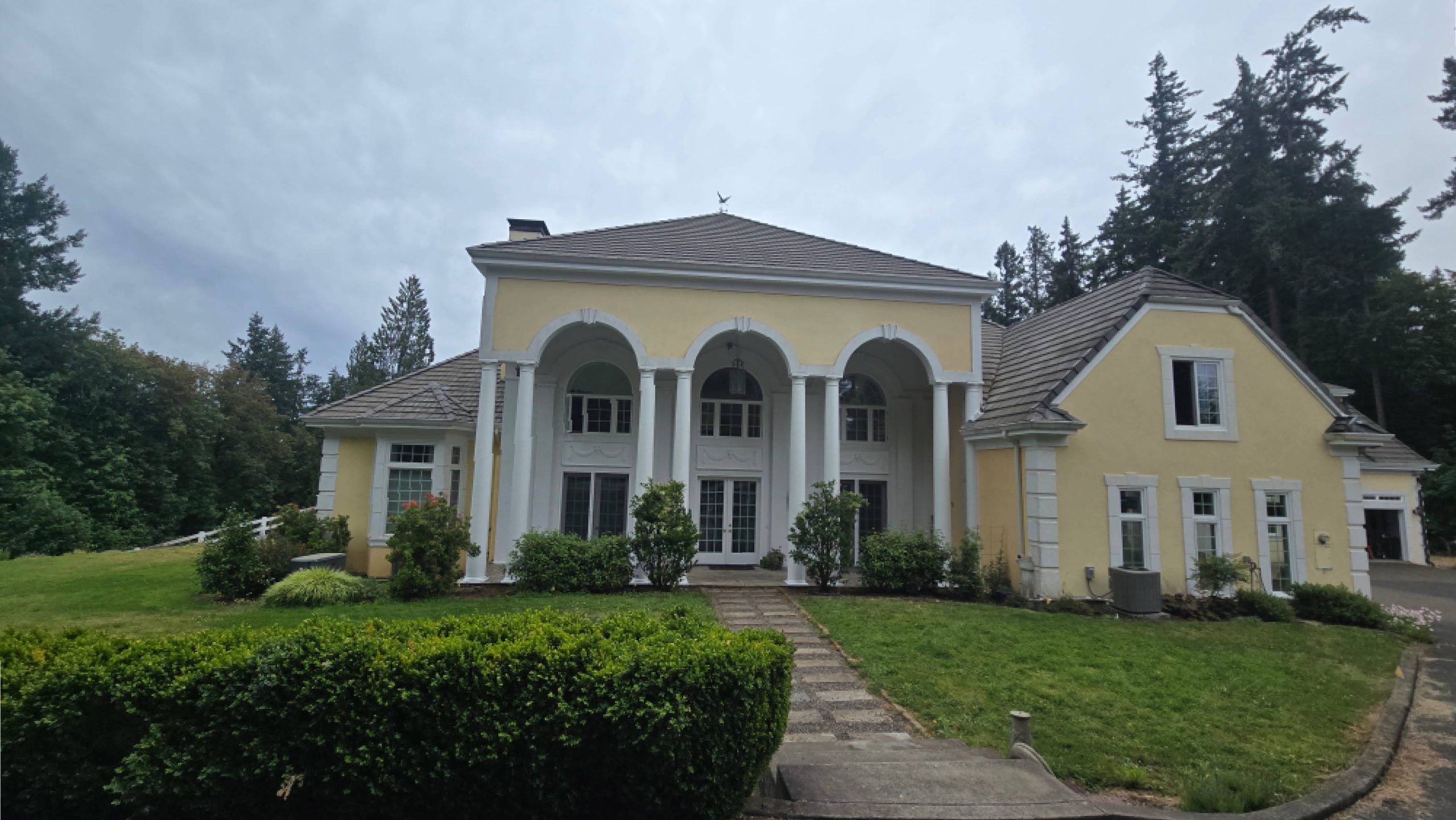 A two-story yellow house with a covered front porch featuring four white columns and arched entryways.